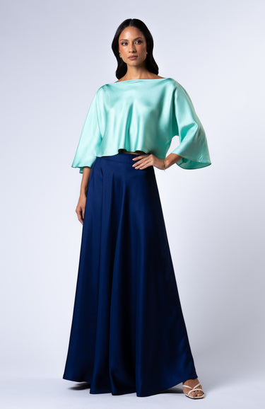 In motion shot of a model wearing the Nicilian Yacht Blouse in Opal and Site Skirt in Beacon Blue, both crafted from regenerative silk twill. This full-length luxury set blends modest elegance with flowing, structured design.