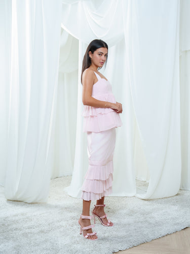 The Cascade Blouse and Cascade Skirt in light pink worn as a set, a tiered silk top above a tiered midi skirt.