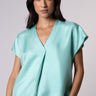 Model wearing Nicilian's Aura Blouse in Opal — a regenerative silk top with cap sleeves, front pleat, and V-neckline.