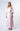 A woman wearing Nicole’s Signature Dress in barely pink silk twill, featuring a V-neckline, silk-covered buttons, bell sleeves, and an adjustable tie waist.